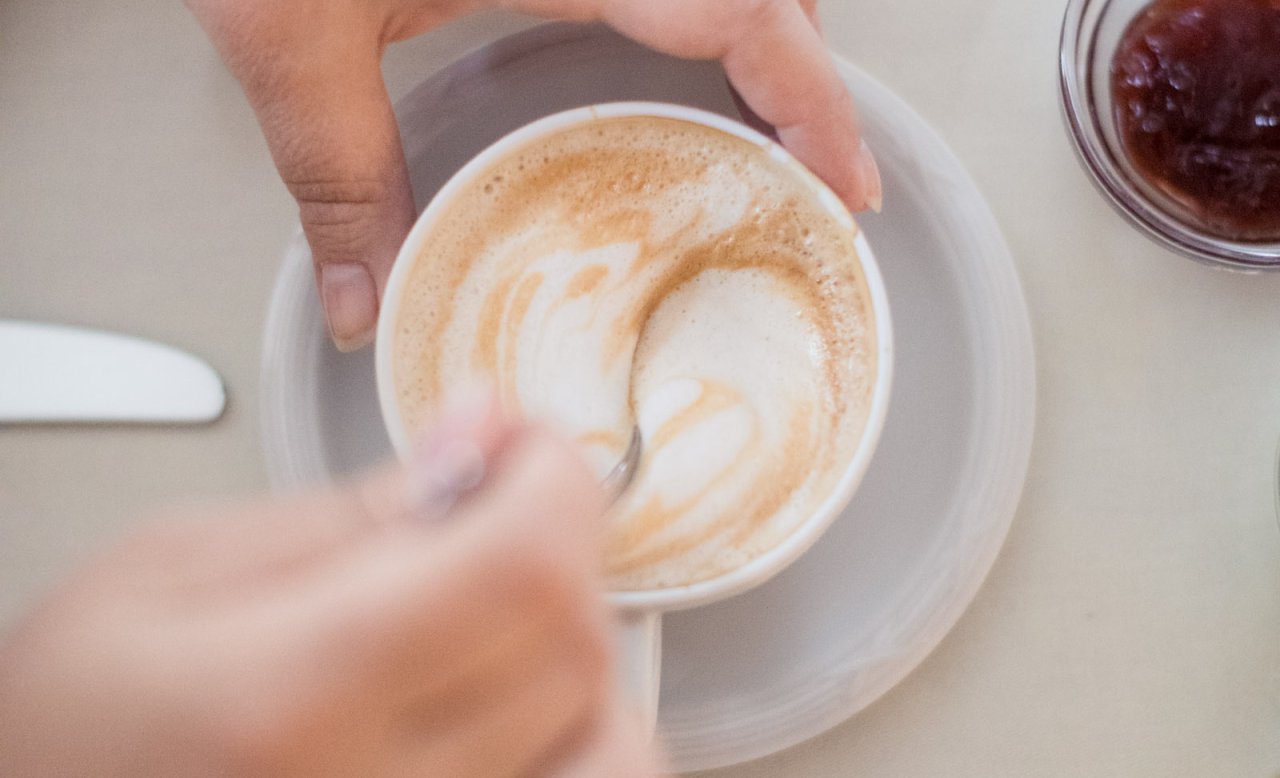 Zwei Hände halten eine Cappuccino-Tasse während der Kaffeepause im Hotel Masatsch