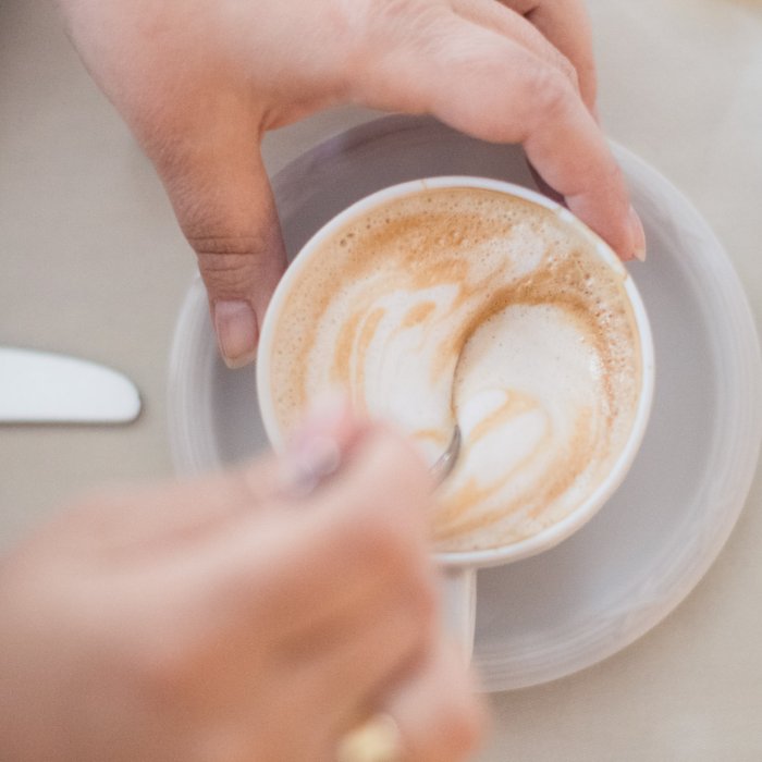 Zwei Hände halten eine Cappuccino-Tasse von oben gesehen im Restaurant Masatsch