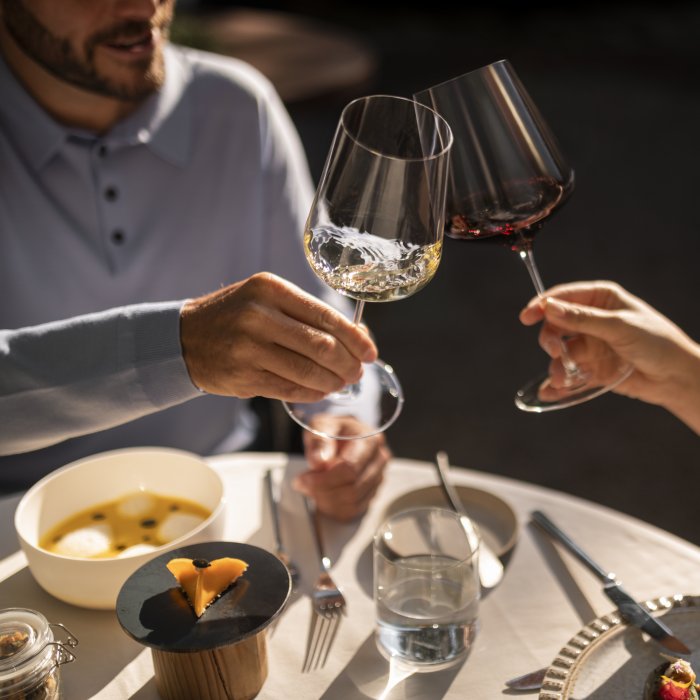 Zwei Hände mit zwei Weingläsern, Rotwein und Weißwein, beim Anstoßen